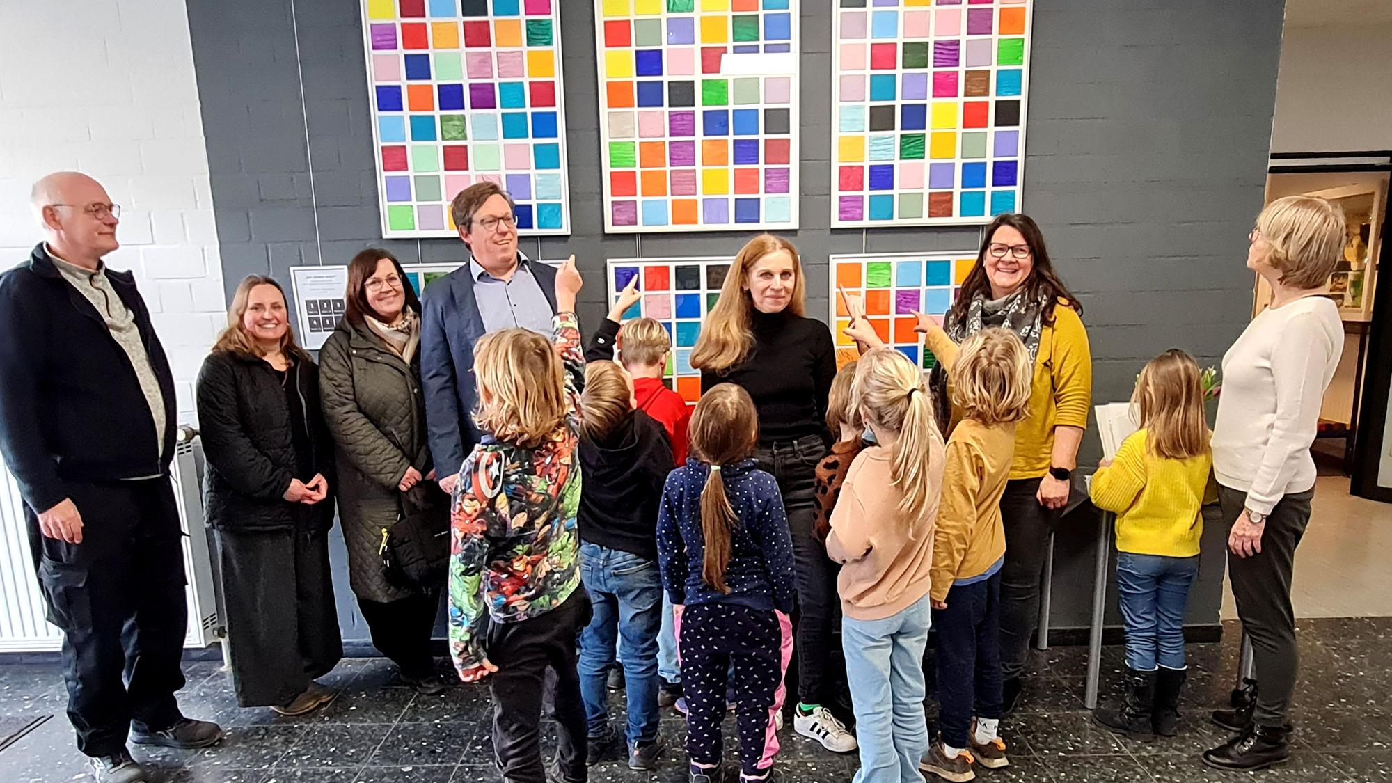 Schüler, Lehr- und OGS-Personal stehen vor dem Kunstprojekt im Foyer der Grundschule.