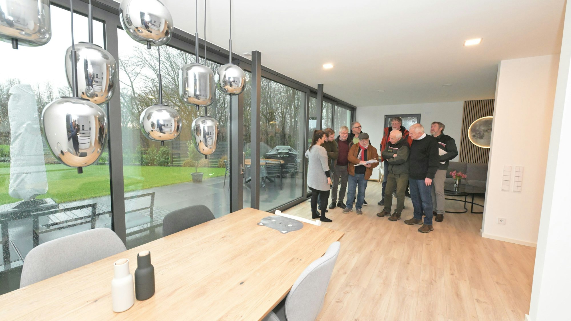 Die Jurymitglieder stehen in einem Wohnzimmer und sind über ein Dokument gebeugt.