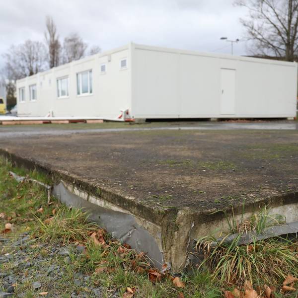 Auf einer großen Bodenplatte steht ein weißer Wohncontainer.