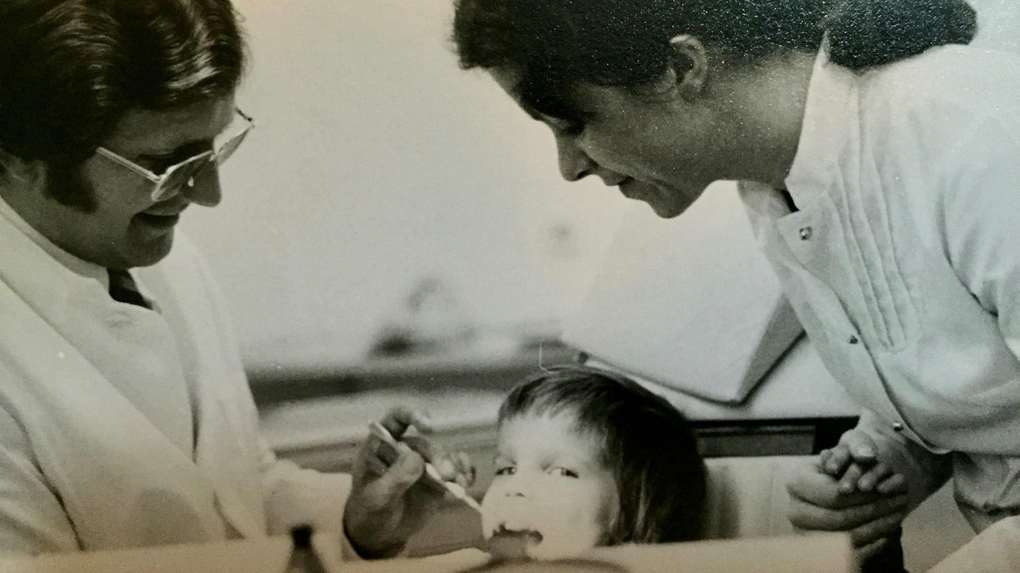 Ein kleiner Junge wird von einem Zahnarzt behandelt. Eine Arzthelferin hält die Hand des Jungen.