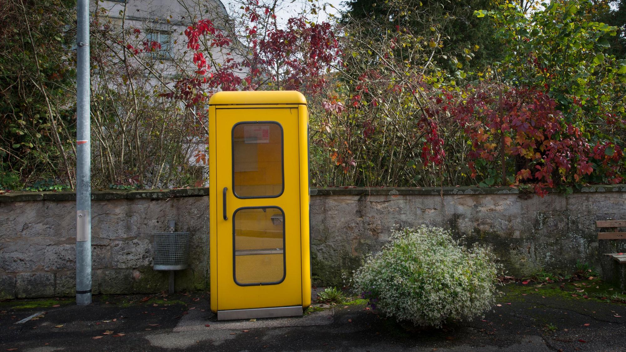 Eine gelbe Telefonzelle steht am Rande einer Straße.