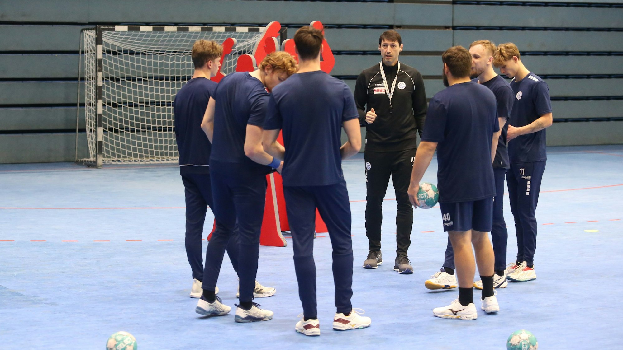 Mehrere Handballspieler des VfL Gummersbach stehen mit ihrem Co-Trainer im Kreis.