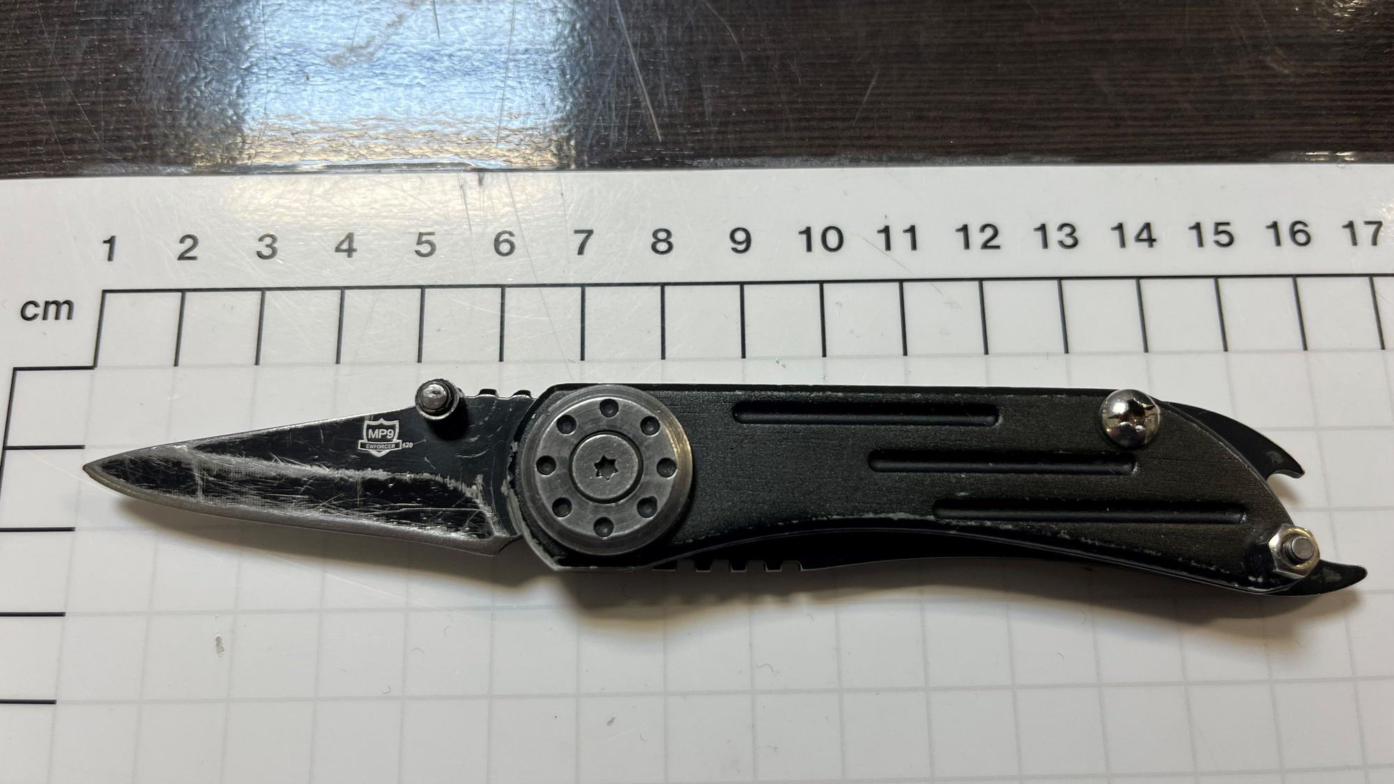 Auf einer Maßtabelle liegt ein schwarzes Messer mit aufgeklappter Klinge.