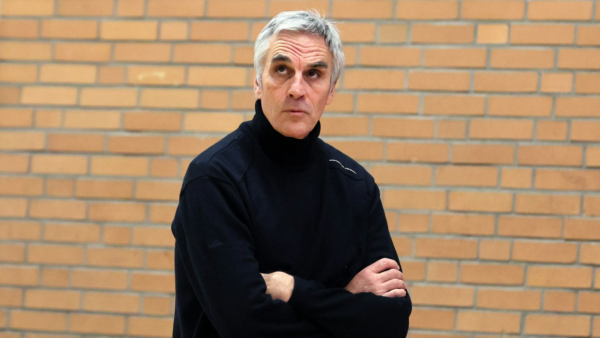 Ein Basketball-Trainer steht mit verschränkten Armen am Spielfeldrand und schaut nach oben.