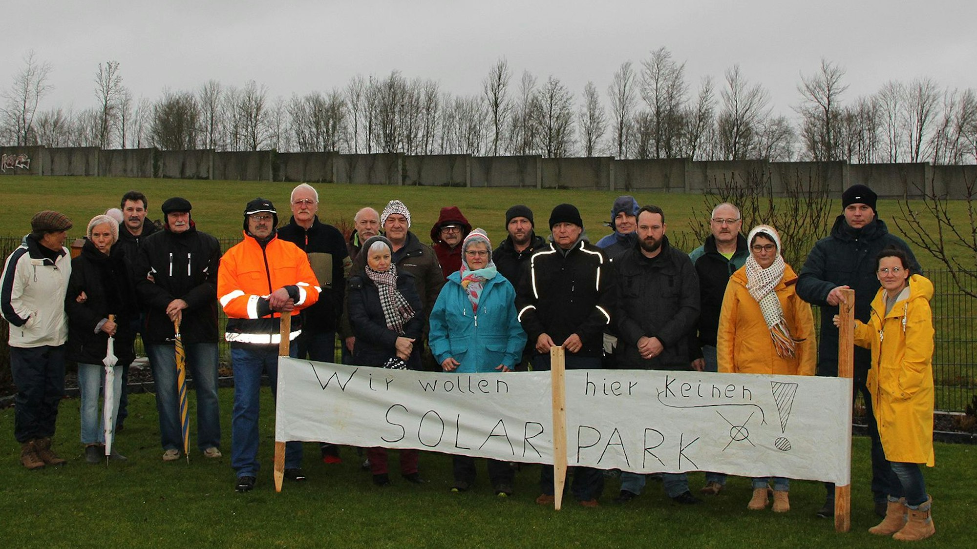 19 Anwohner haben sich mit einem Protestbanner vor der Fläche postiert, auf der ein Teil des Dahlemer Solarparks geplant ist. Auf dem Banner steht: „Wir wollen hier keinen Solarpark.“