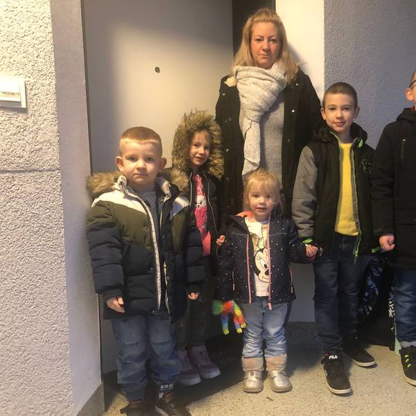 Eine Mutter mit fünf Kindern steht vor einer Wohnung.