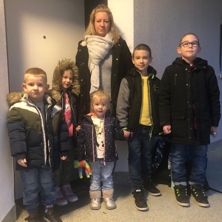 Eine Mutter mit fünf Kindern steht vor einer Wohnung.