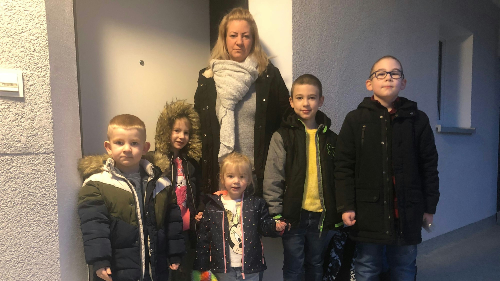 Eine Mutter mit fünf Kindern steht vor einer Wohnung.