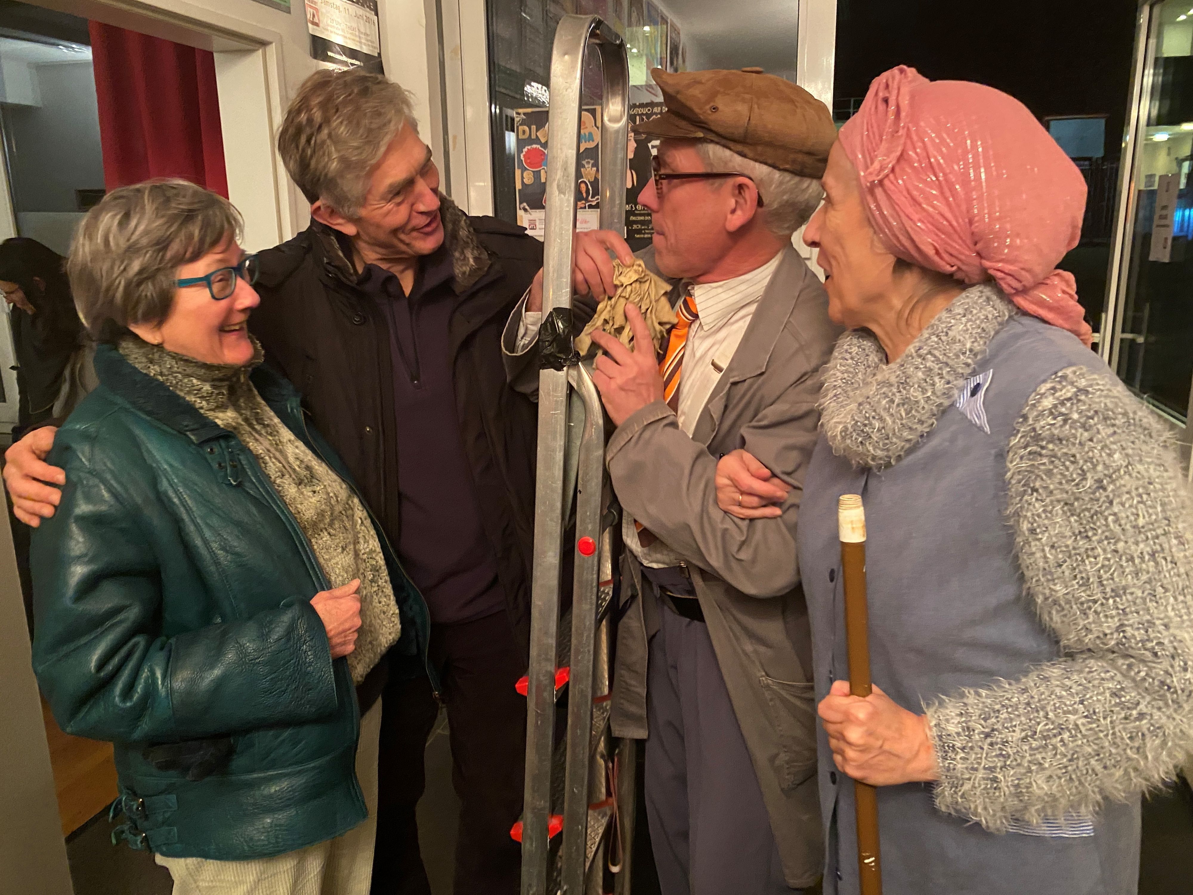 Udo Passon und Inge Weyberg stehen als Hausmeister mit Leiter und Putzfrau bei zwei Gästen.
