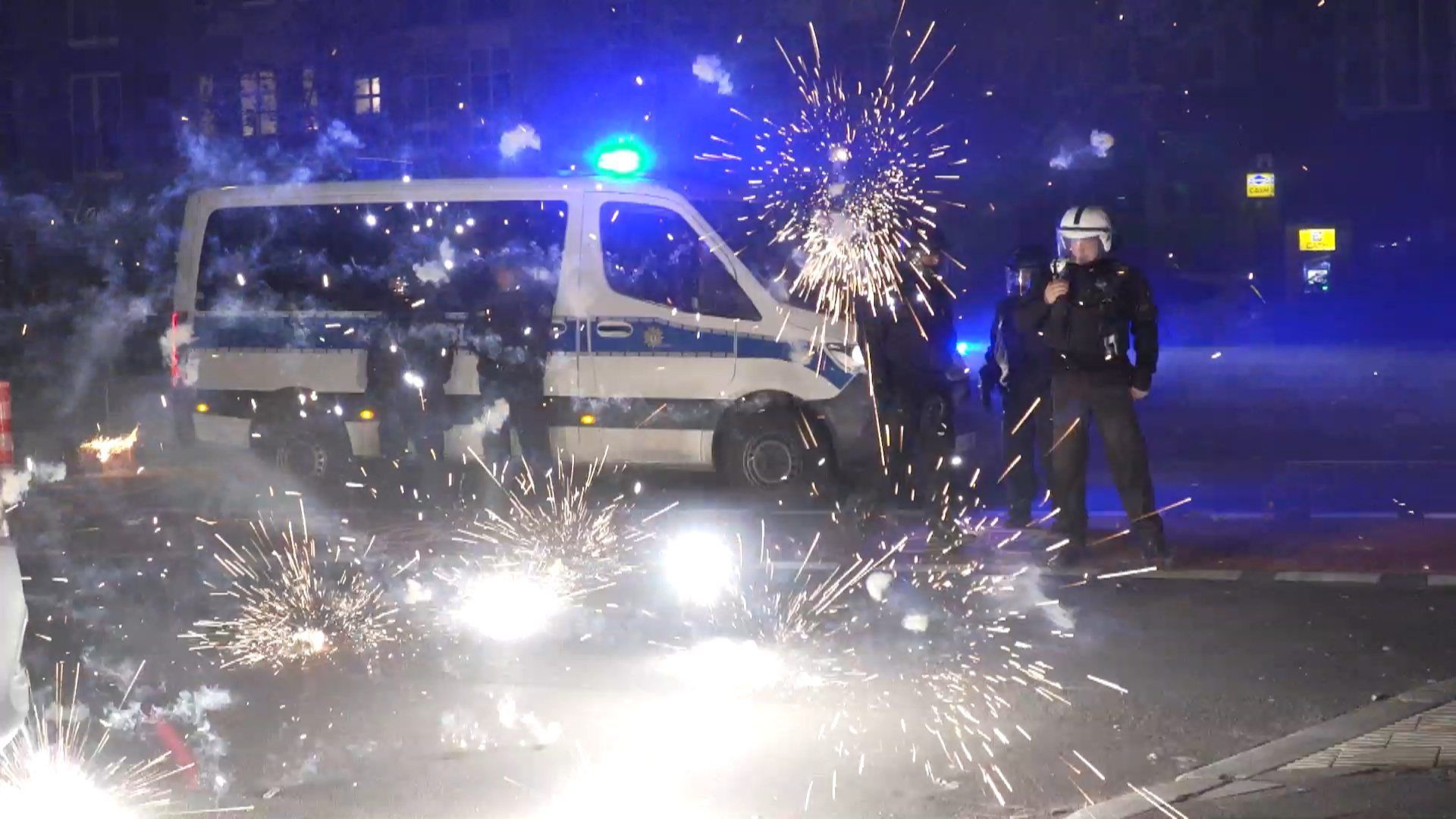 31.12.2022, Berlin: Polizeibeamte stehen hinter explodierendem Feuerwerk.
