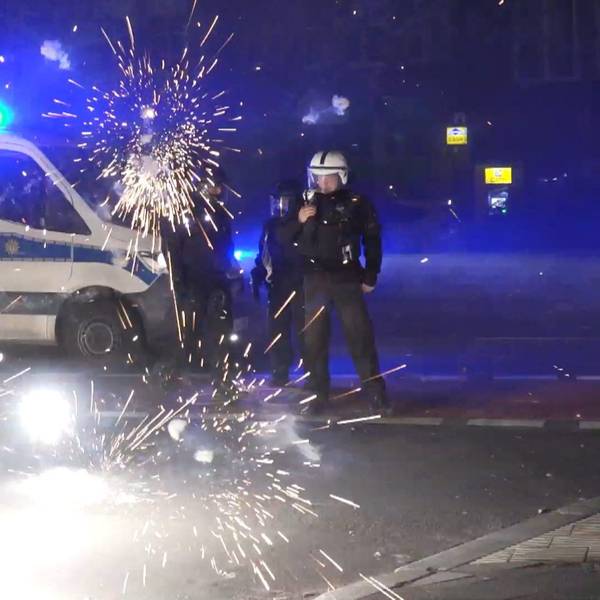 31.12.2022, Berlin: Polizeibeamte stehen hinter explodierendem Feuerwerk.