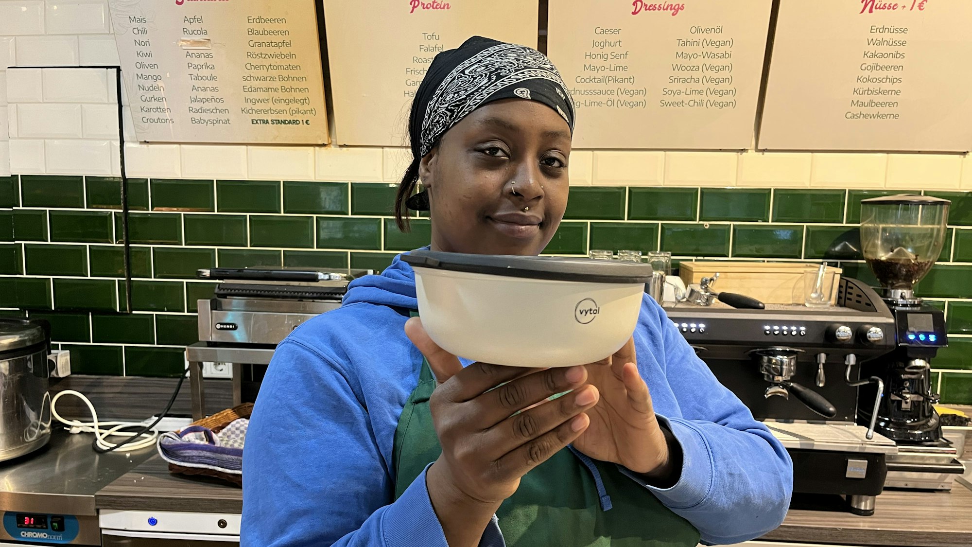 Eine Frau in einem Restaurant zeigt eine Schüssel des Kölner Mehrweg-Anbieters Vytal.