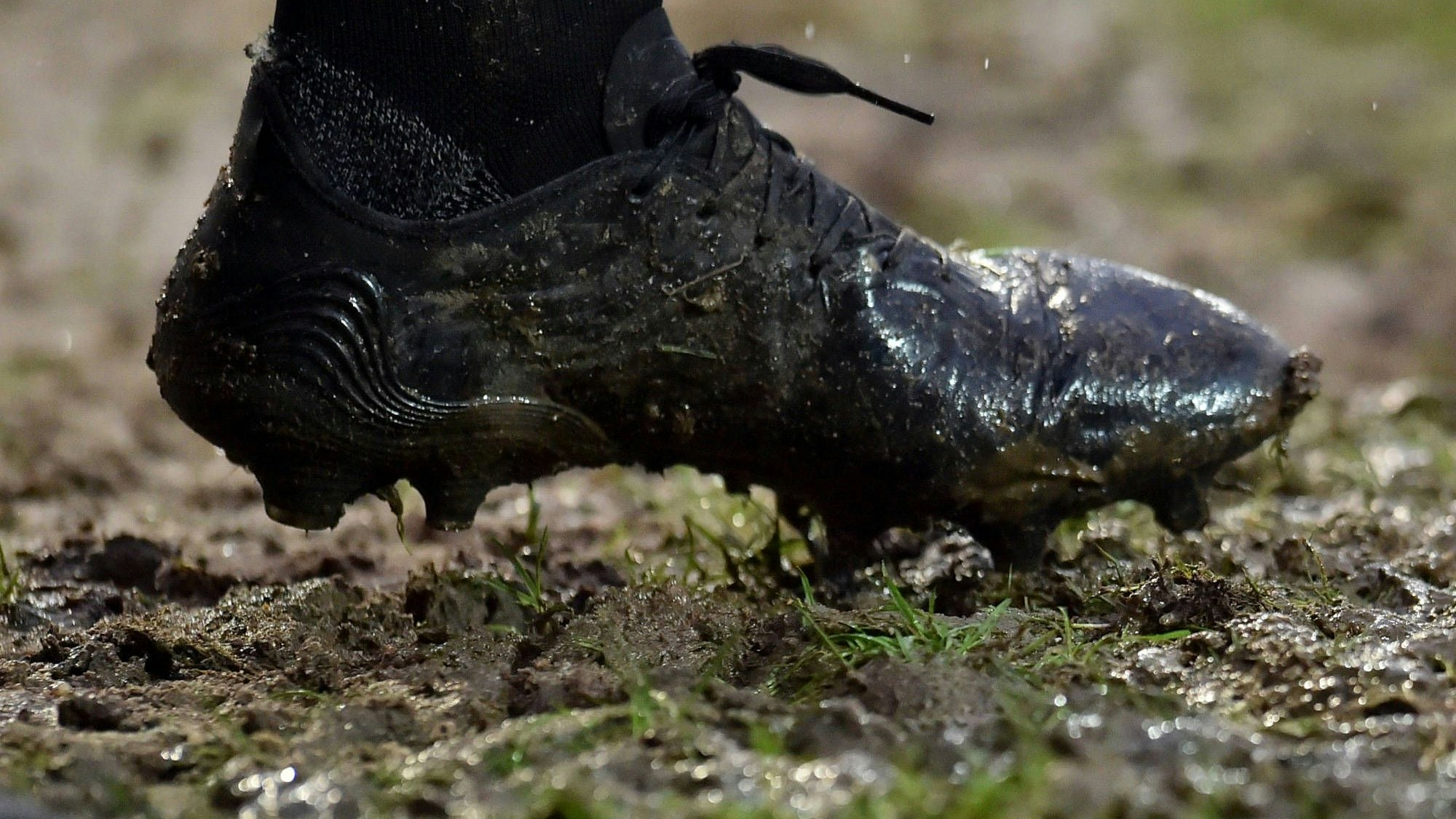 Bild eines mit Matsch verschmierten Fußballschuhs auf einem schlammigen Rasen