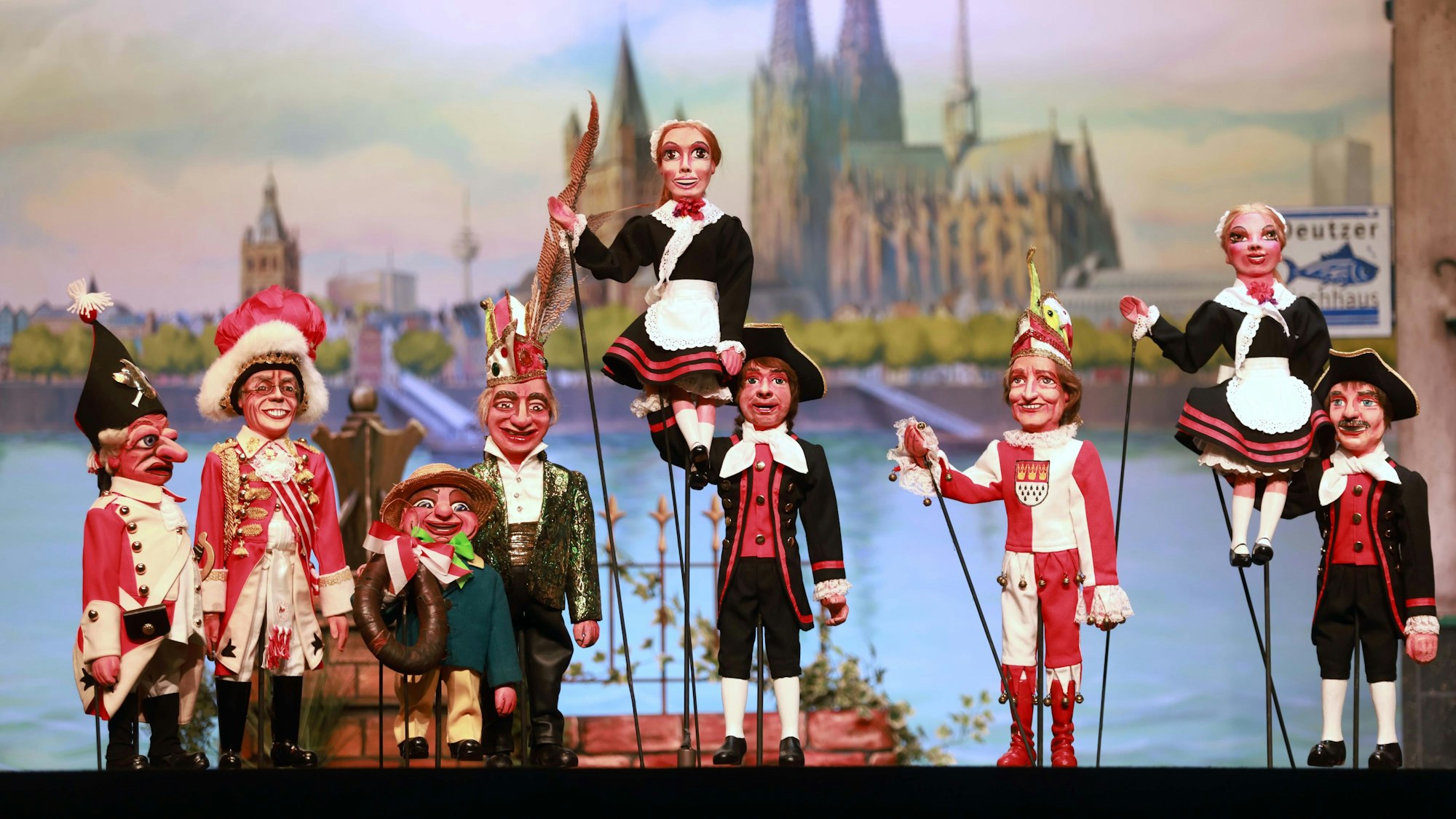 Verschiedene Puppen stehen vor einer Leinwand, die den Kölner Dom abbildet.