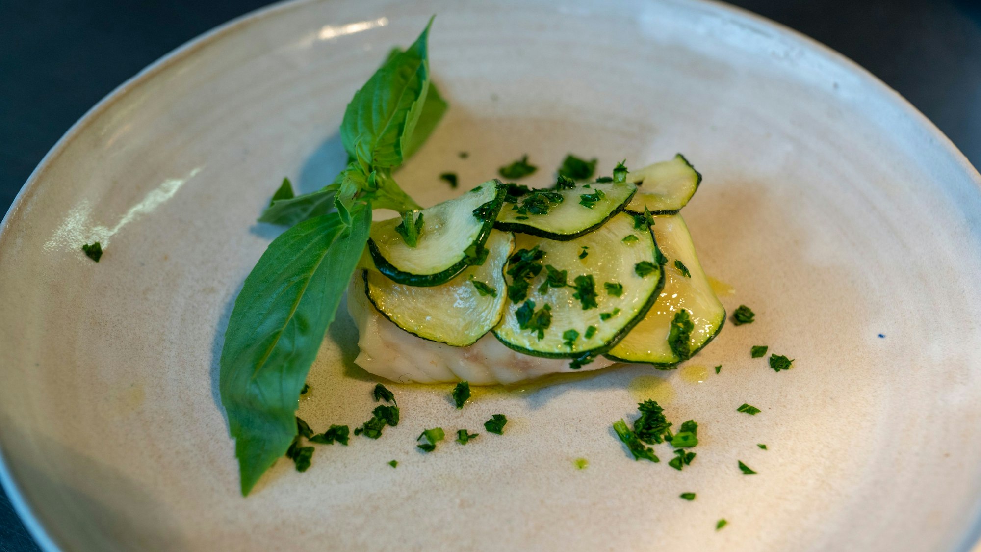 von Zucchini bedecktes Stück Fisch auf einem Teller