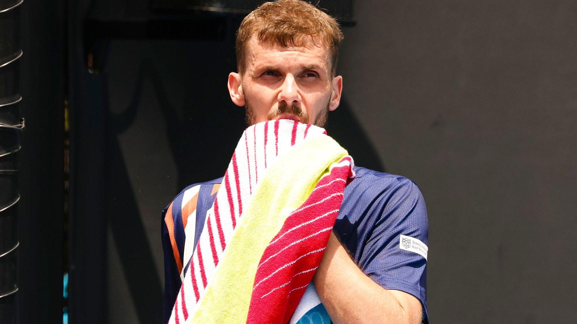 Tennisprofi Oscar Otte wischt sich mit einem Handtuch durchs Gesicht.