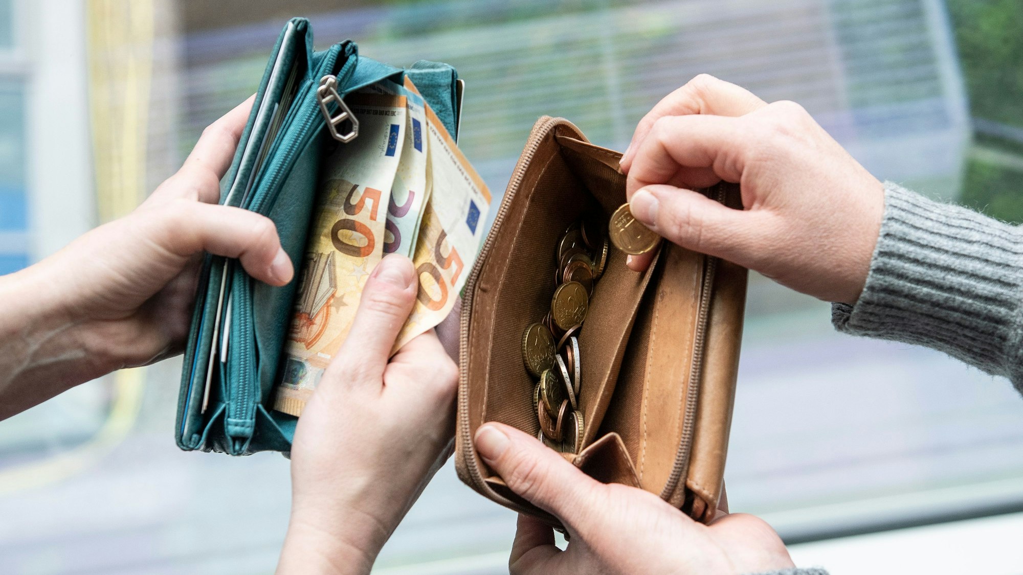 Zwei Menschen zeigen den Inhalt ihrer Geldbeutel. In einem sind Euro-Scheine (50er und 20er), im anderen nur Münzen.