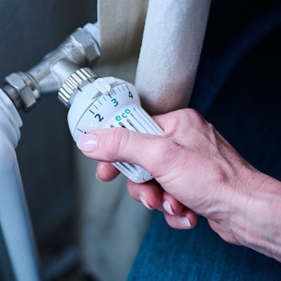 Eine Hand dreht am Thermostat einer Heizung