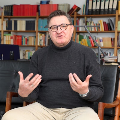 Norbert Hörter sitzt vor einer Bücherwand und gestikuliert.