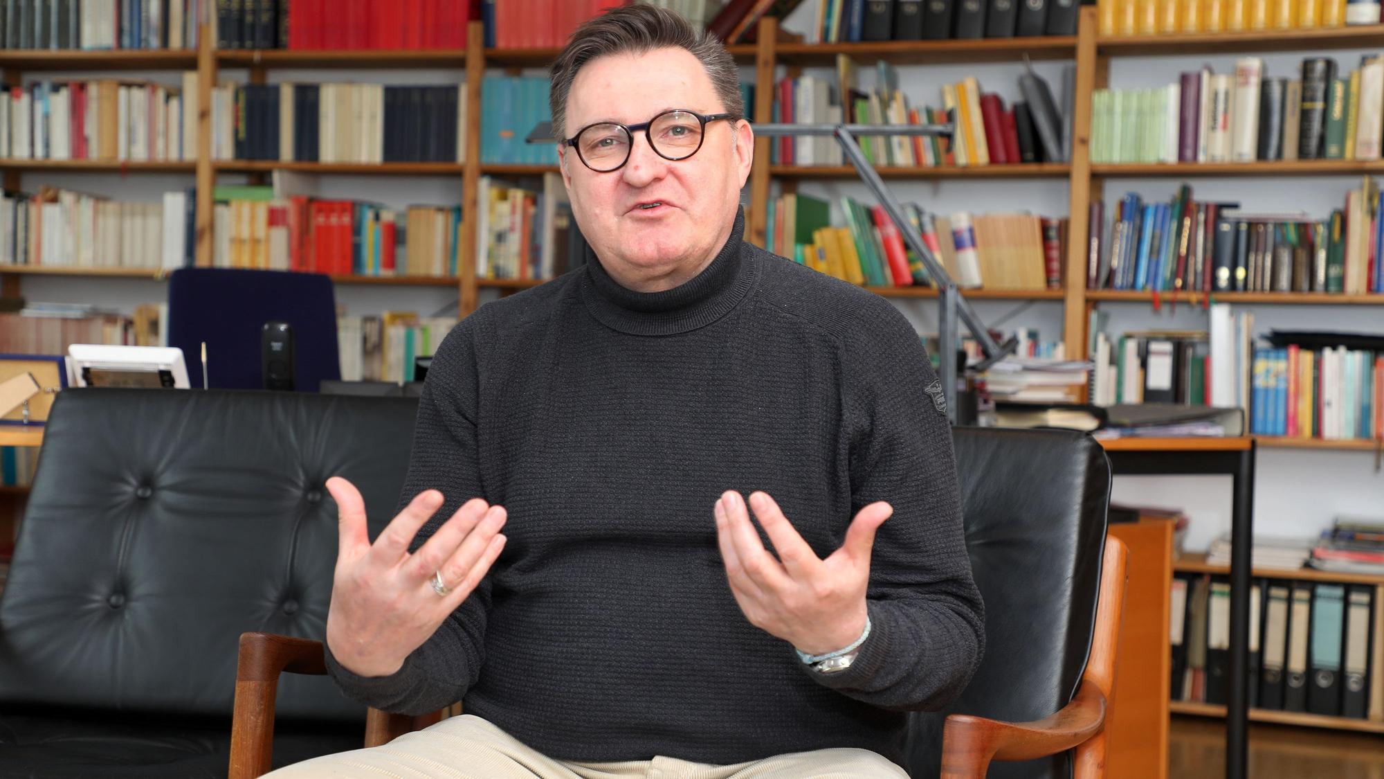 Norbert Hörter sitzt vor einer Bücherwand und gestikuliert.