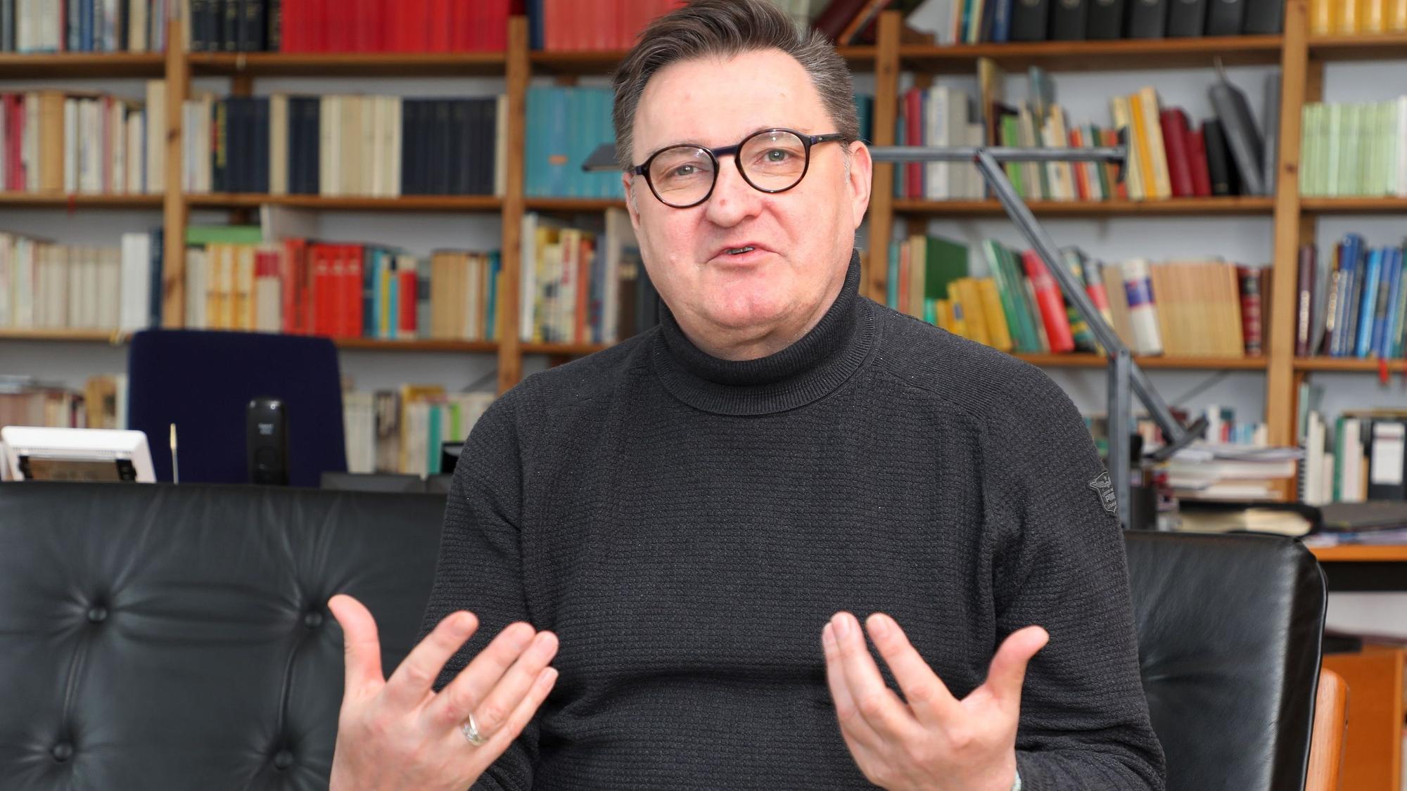 Der katholische Pfarrer und Kreisdechant Norbert Hörter sitzt in einem Sessel seines Arbeitszimmers vor einer Bücherwand und spricht.