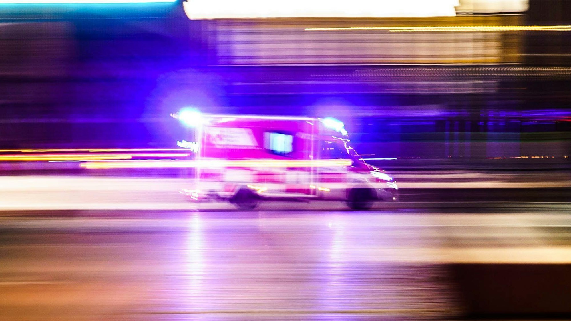 Ein Rettungsfahrzeug ist vor Tagesanbruch mit Blaulicht unterwegs (Aufnahme mit Mitzieheffekt).