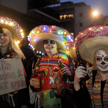Drei als Geister geschminkte Menschen mit Sombreros mit Lichterketten.