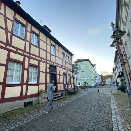 Ein Mann geht in einer Gasse über Kopfsteinpflaster an einem Fachwerkhaus vorbei.