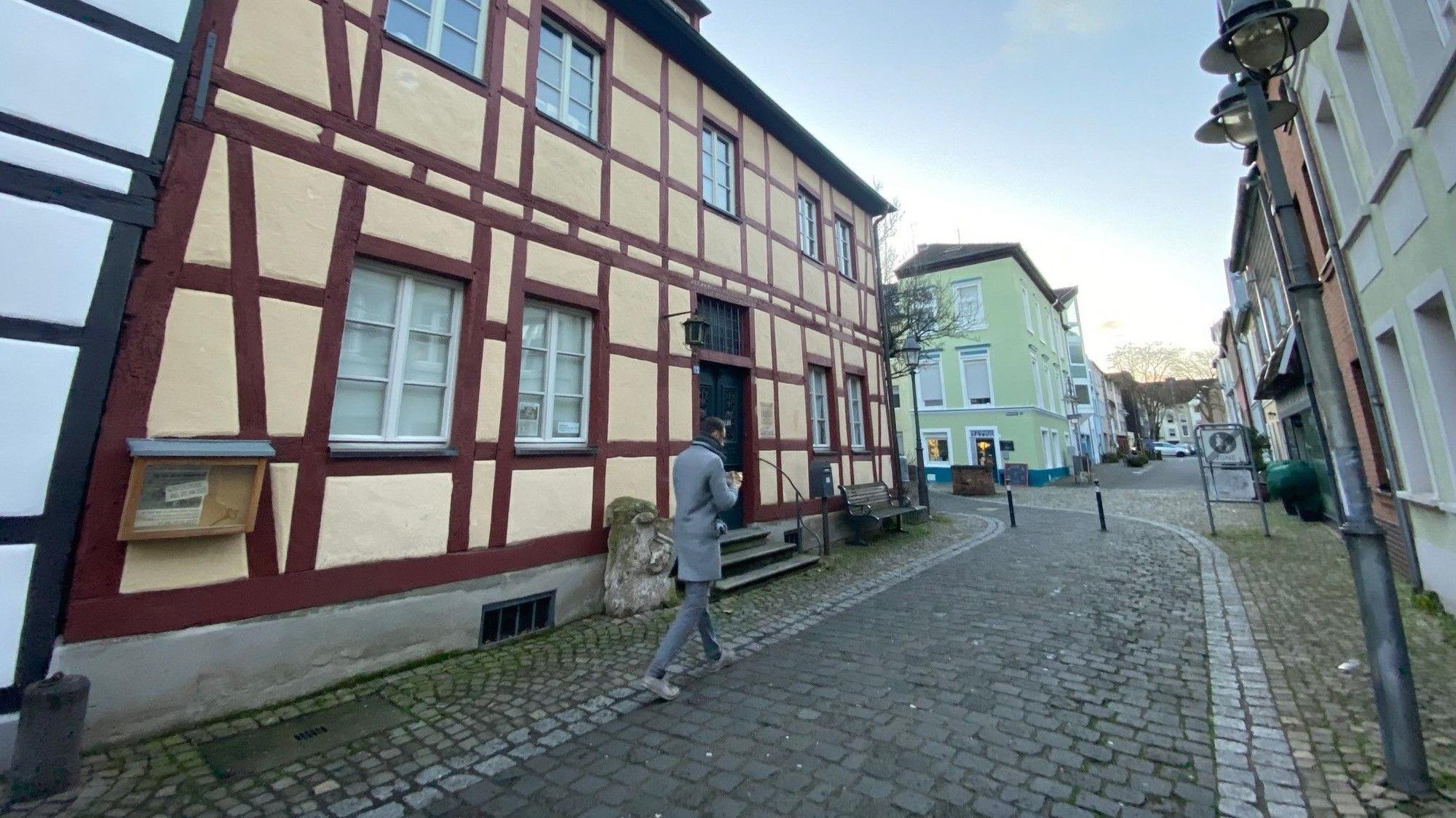 Ein Mann geht in einer Gasse über Kopfsteinpflaster an einem Fachwerkhaus vorbei.