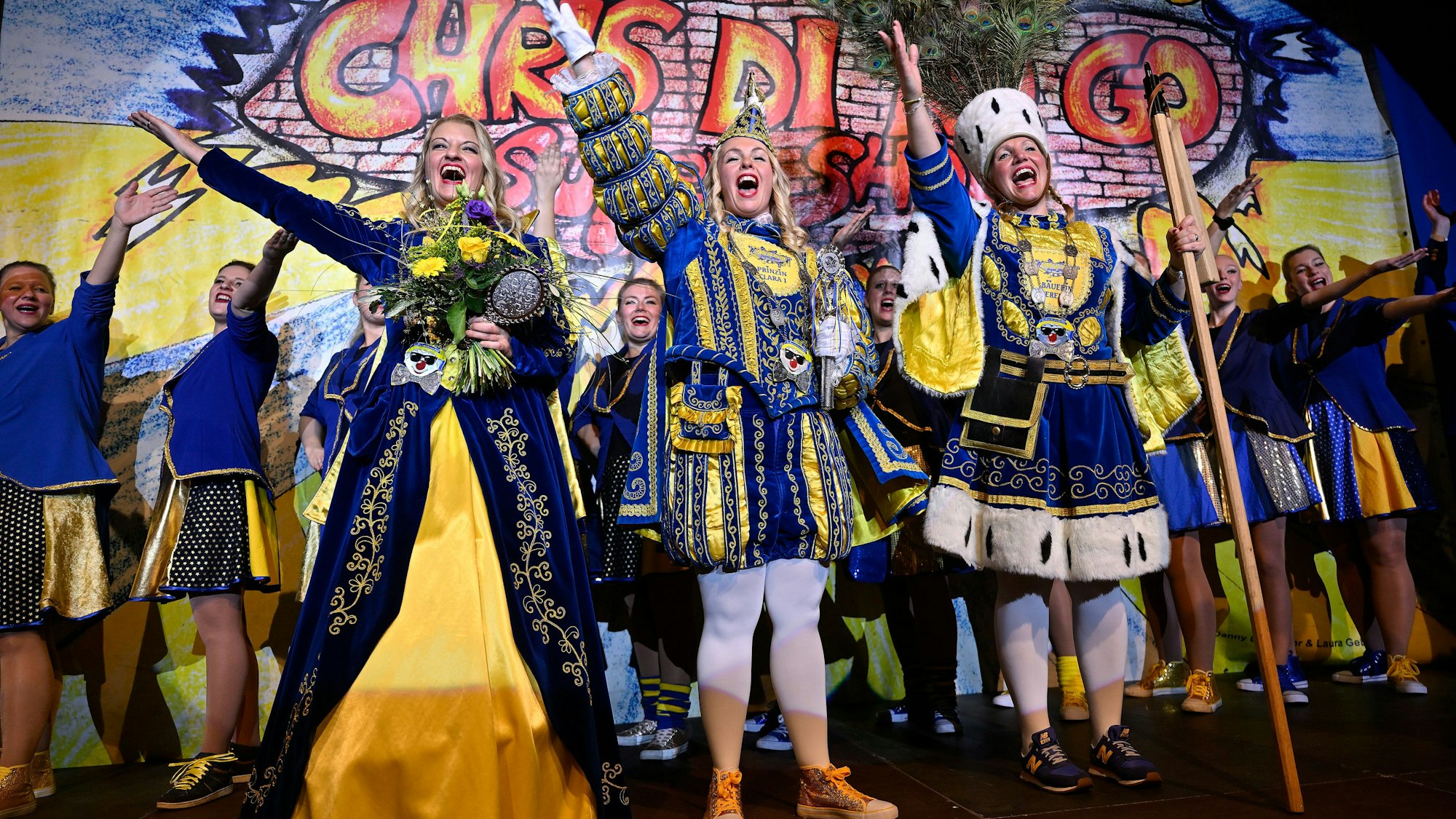 Prinz*in Clara I. (Brückers, Mitte), Bäuerin Verena (von Mengden, rechts) und Jungfrau Inga (Schoppeit) stehen auf der Bühne und jubeln.