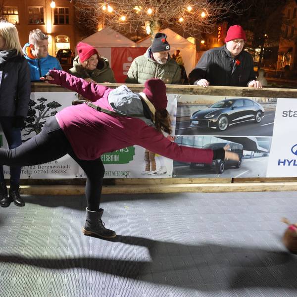 Zu sehen ist die Kunststoffbahn, die beim Bergneustädter Wintermärchen die Eisbahn ersetzt. Im Vordergrund wirft eine Frau mit dicker Jacke, Schal und Mütze einen Eisstock.