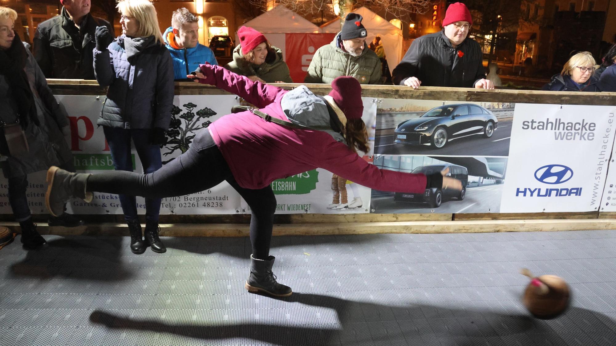 Zu sehen ist die Kunststoffbahn, die beim Bergneustädter Wintermärchen die Eisbahn ersetzt. Im Vordergrund wirft eine Frau mit dicker Jacke, Schal und Mütze einen Eisstock.