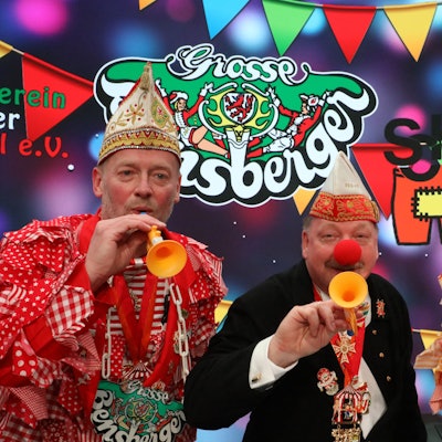 Rainer Furth-Quernheim (Große Bensberger), Harald Hahn (Förderverein Refrather Karneval) und Schlader-Botze-Chef Michael „Mio“ Oppermann (v.l.) stehen in Karnevalsklamotten mit bunten Tröten vor buntem Hintergrund.