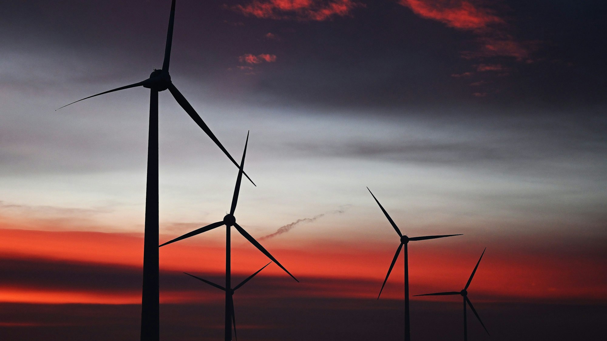 Windräder sind in einem Windpark bei Sonnenaufgang zu sehen.