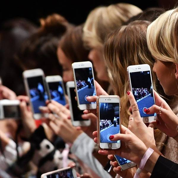 Frauen mit Smartphones filmen und fotografieren eine Modenschau.