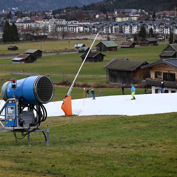 Schneekanonen stehen im Grünen neben einer Skipiste.
