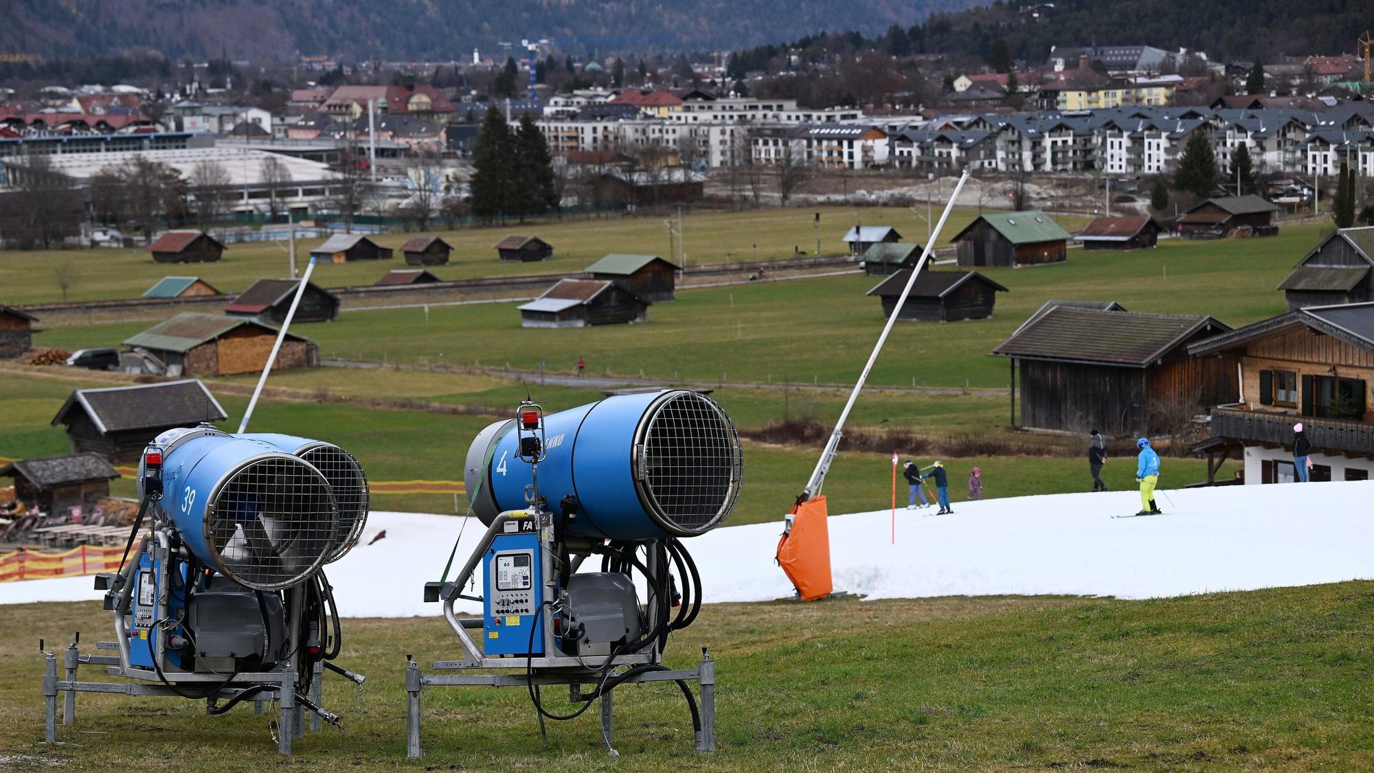 Schneekanonen stehen im Grünen neben einer Skipiste.