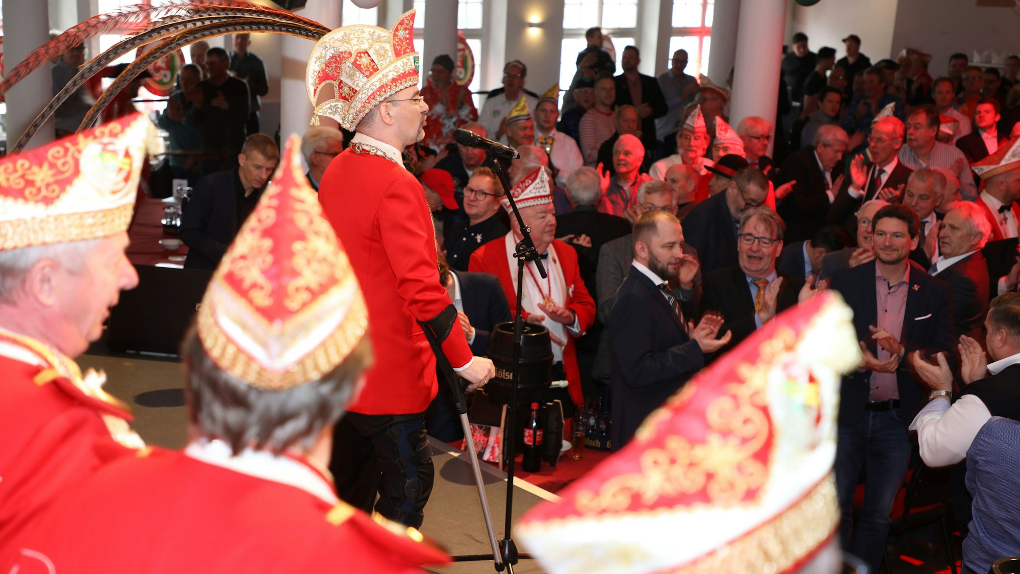 Alexander Pfister steht mit Krücken vor einem Mikro auf einer Karnevalsbühne.