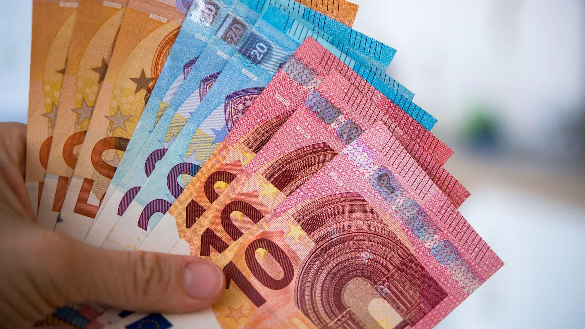 Eine Person hält Banknoten von 10, 20 und 50 Euro gefächert in der Hand (Symbolbild).