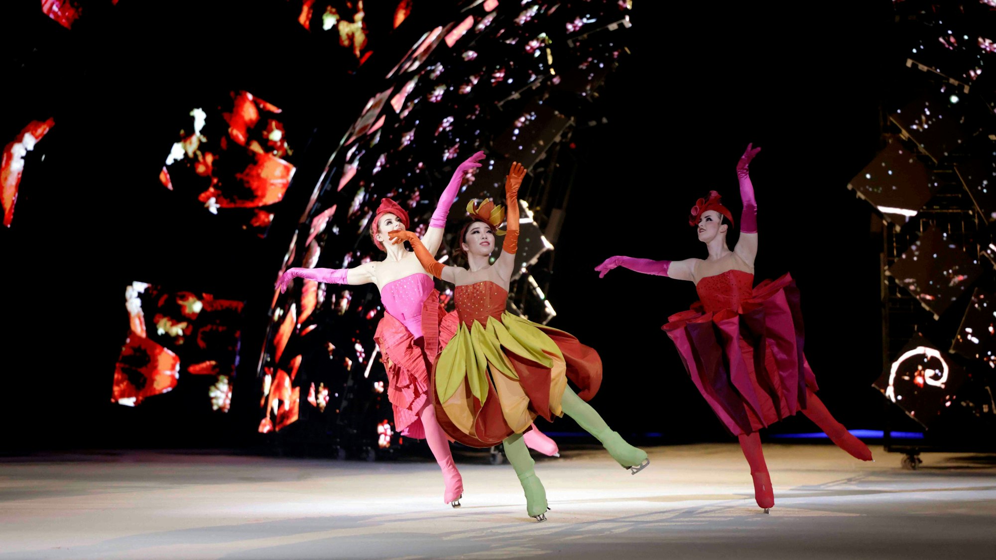 Eiskunstläufer der Show in farbenfrohen Kleidern. Im Hintergrund Farb- und Lichteffekte.