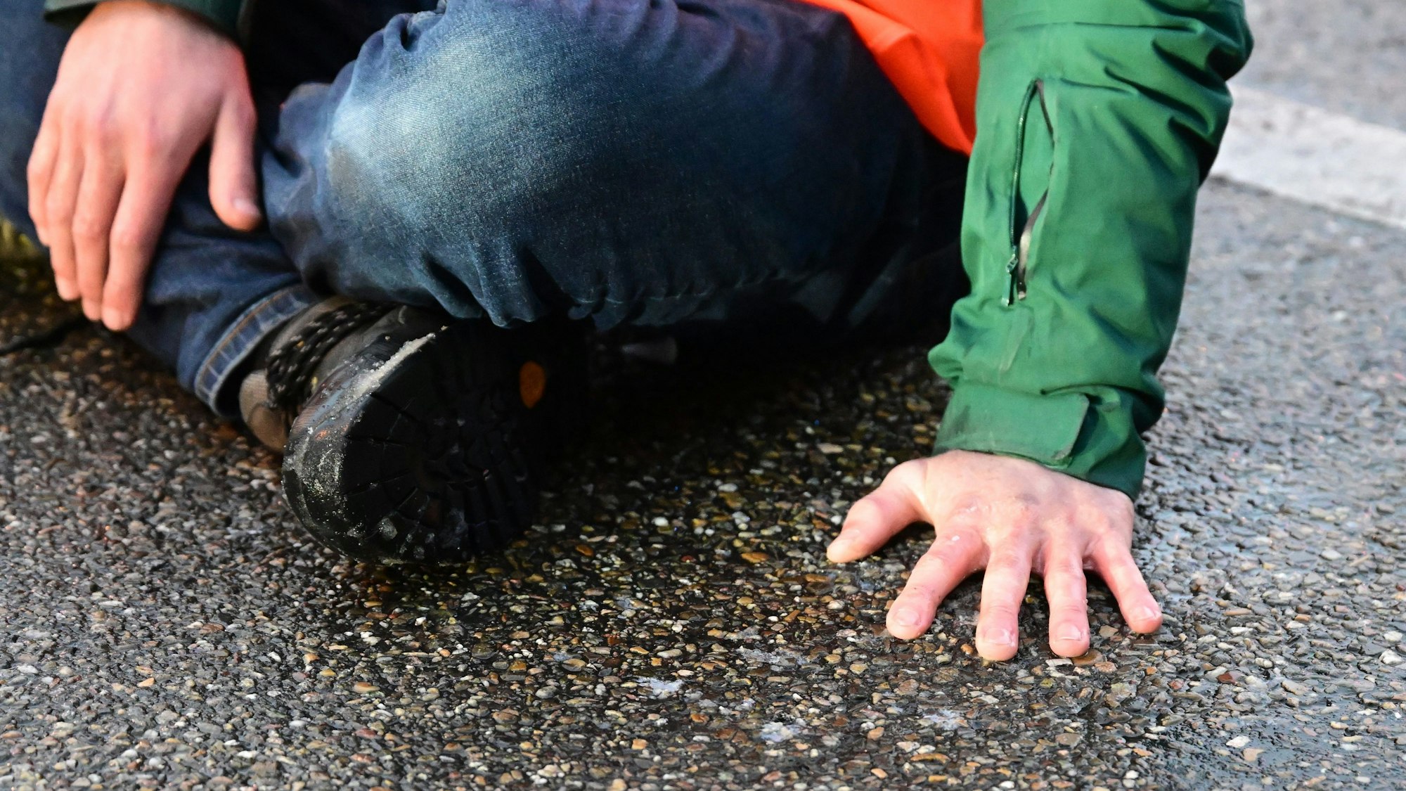 Man sieht eine Hand, die auf einer Straße klebt, die Person ist nicht ganz zu sehen.
