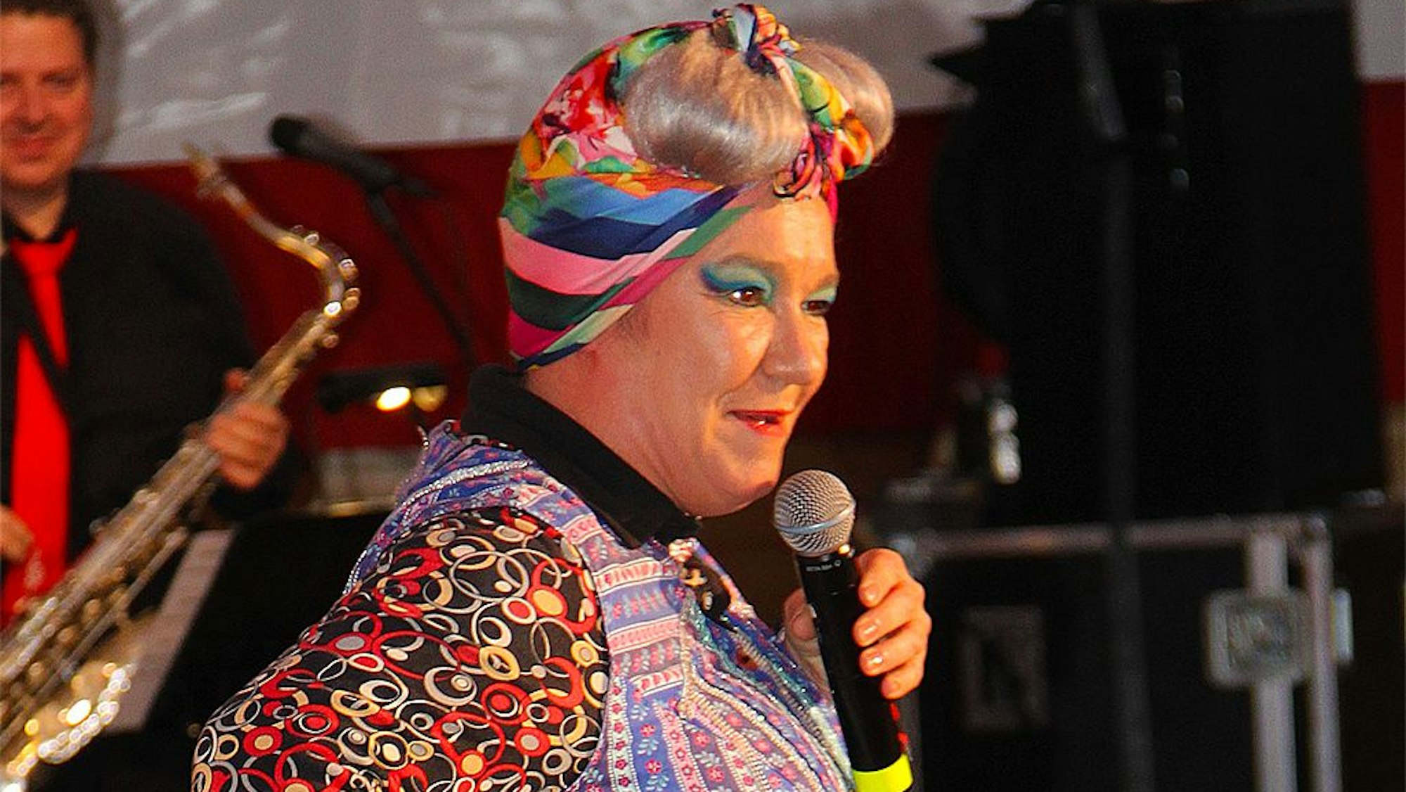 Annette Esser tritt als die resolute Putzfrau Achnes Kasulke mit klassischer Kittelschürze auf.