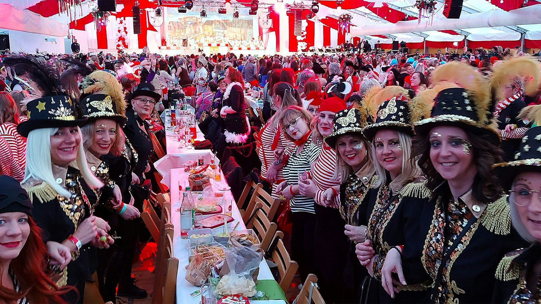 Kostümierte Damen stehen im Festzelt an einem Tisch und haben sich zum Schunkeln untergehakt.