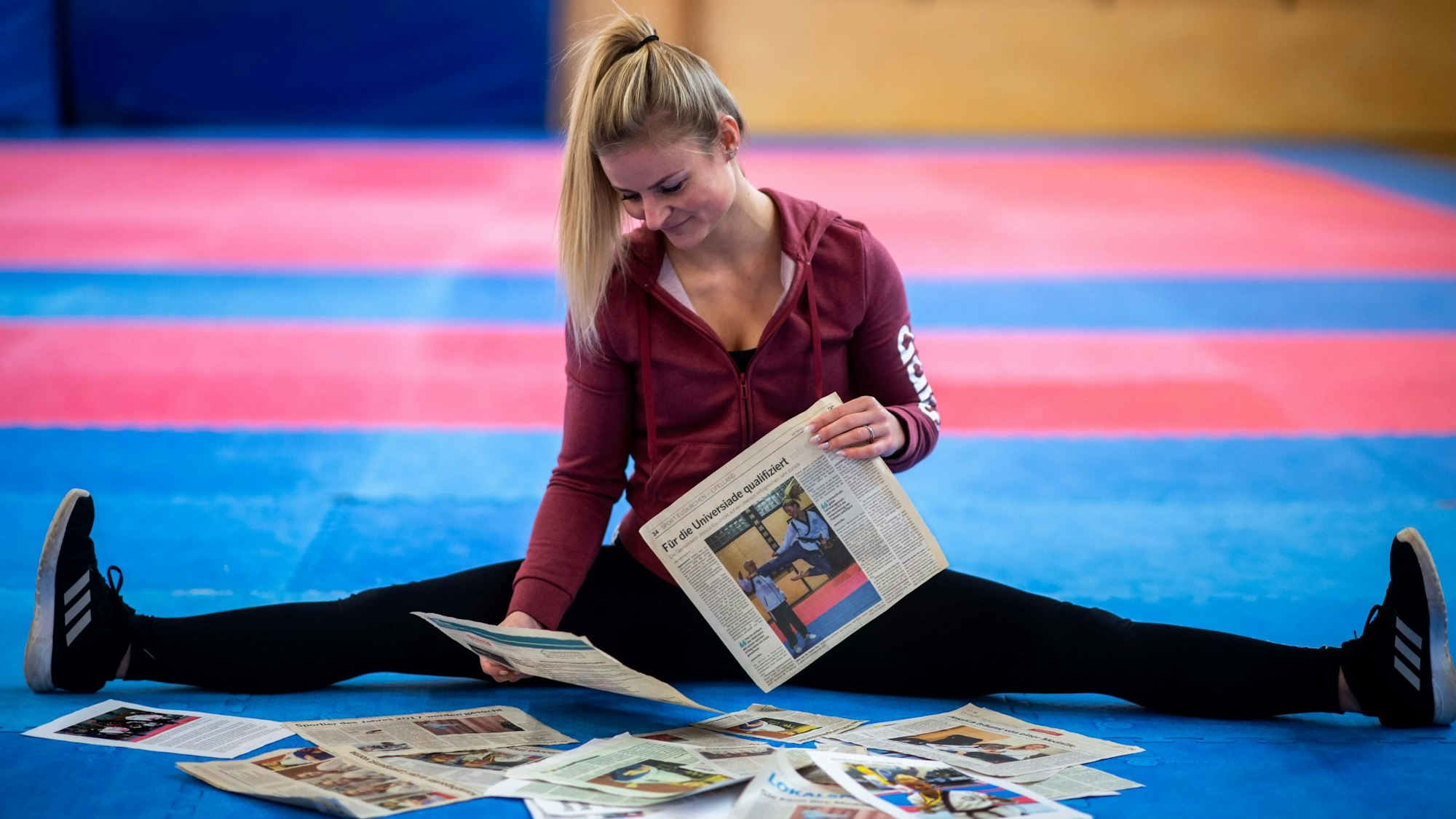 Kampfsportlerin Jessica Rau sitzt in ihrer Trainingshalle auf dem Boden und betrachtet Zeitungsartikel.