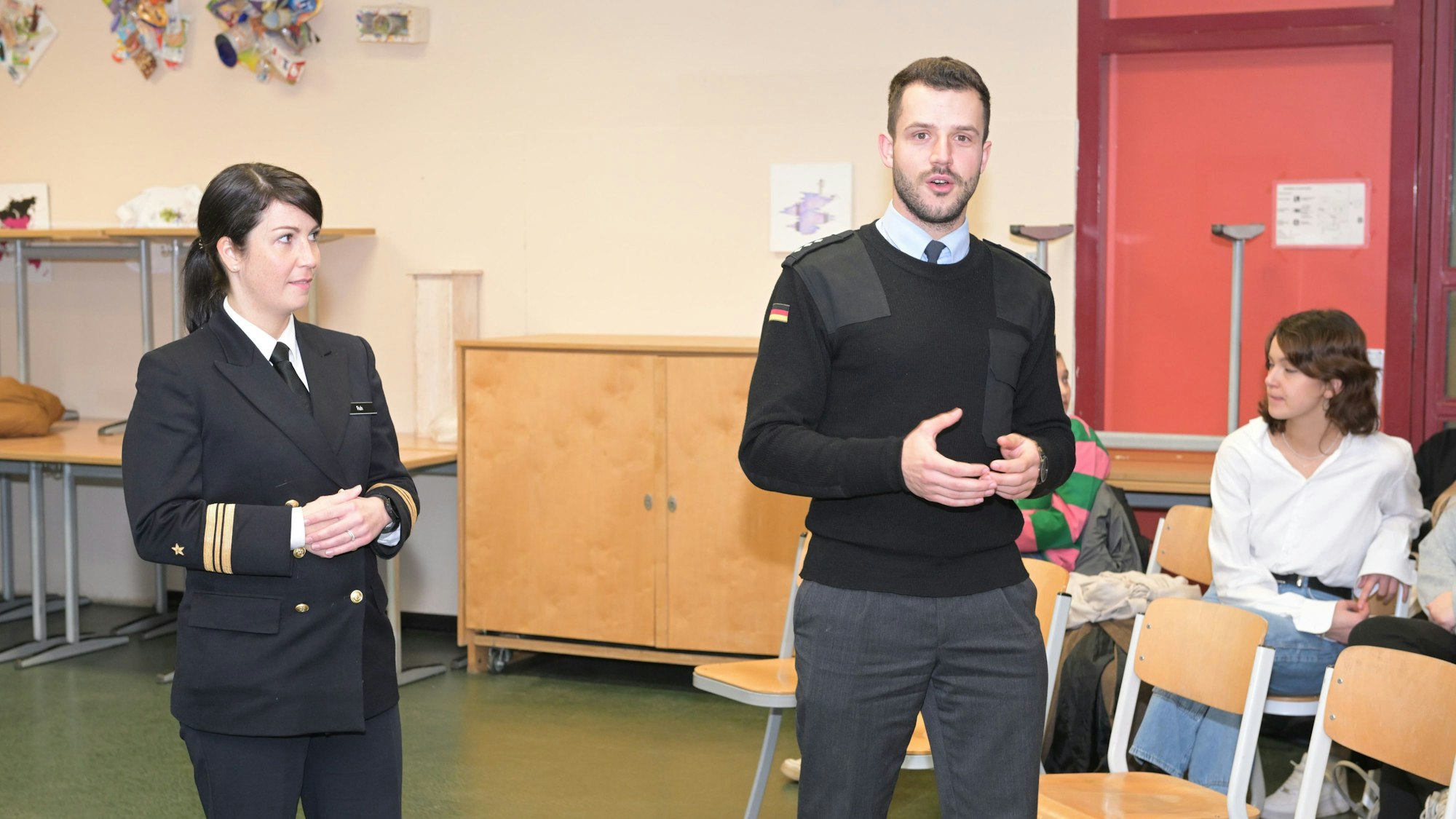 Eine Soldatin und ein Soldat sprechen vor einer Klasse.