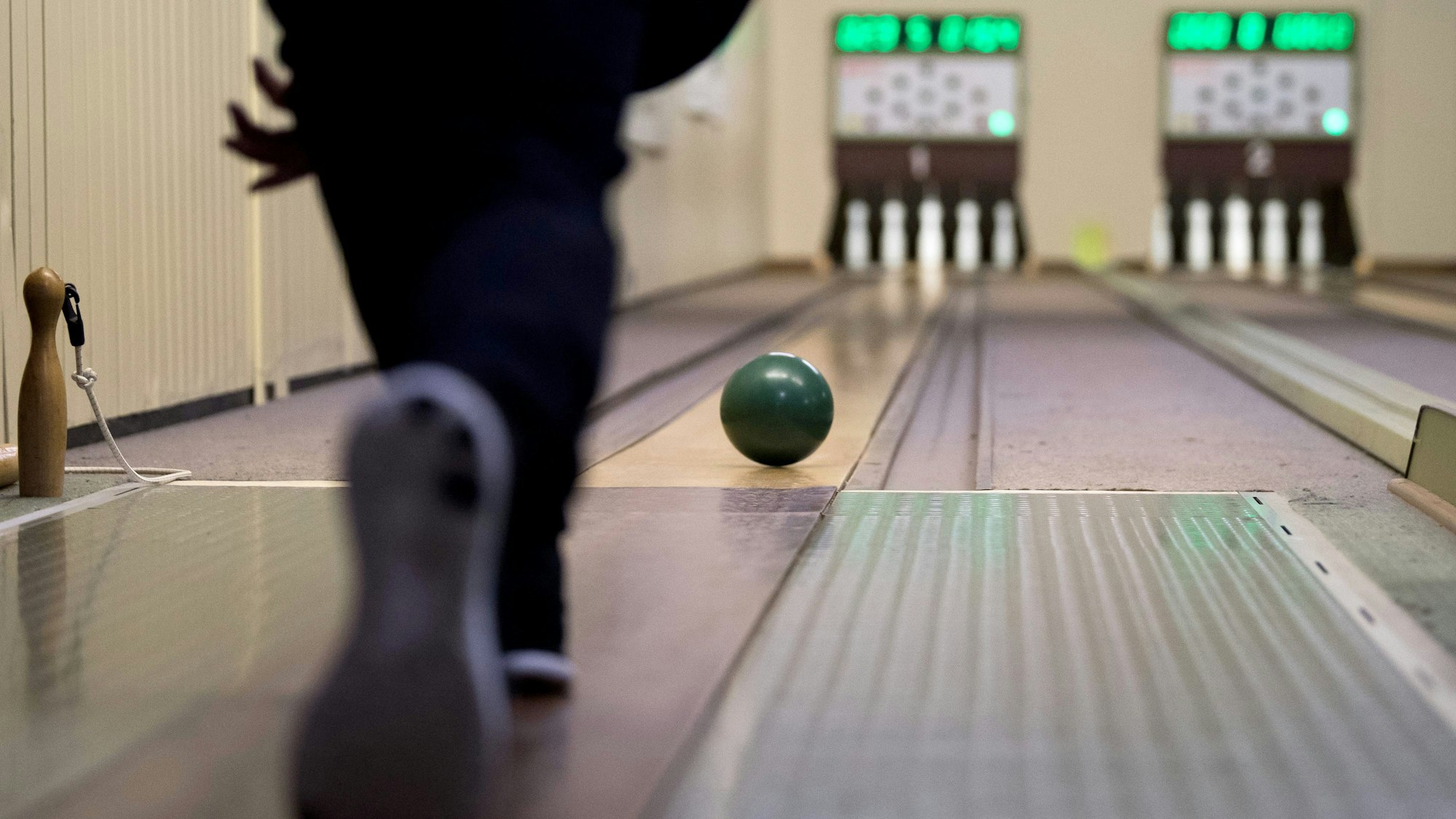 Eine Person spielt die Kugel auf die Bahn in Richtung der neun Kegel.