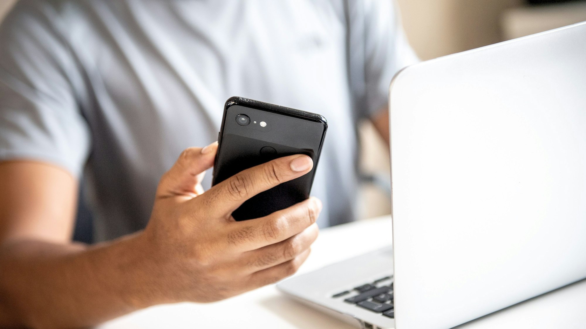 Mann sitzt vor seinem aufgeklappten Laptop und hält in der einen Hand ein Smartphone. (Symbolbild)