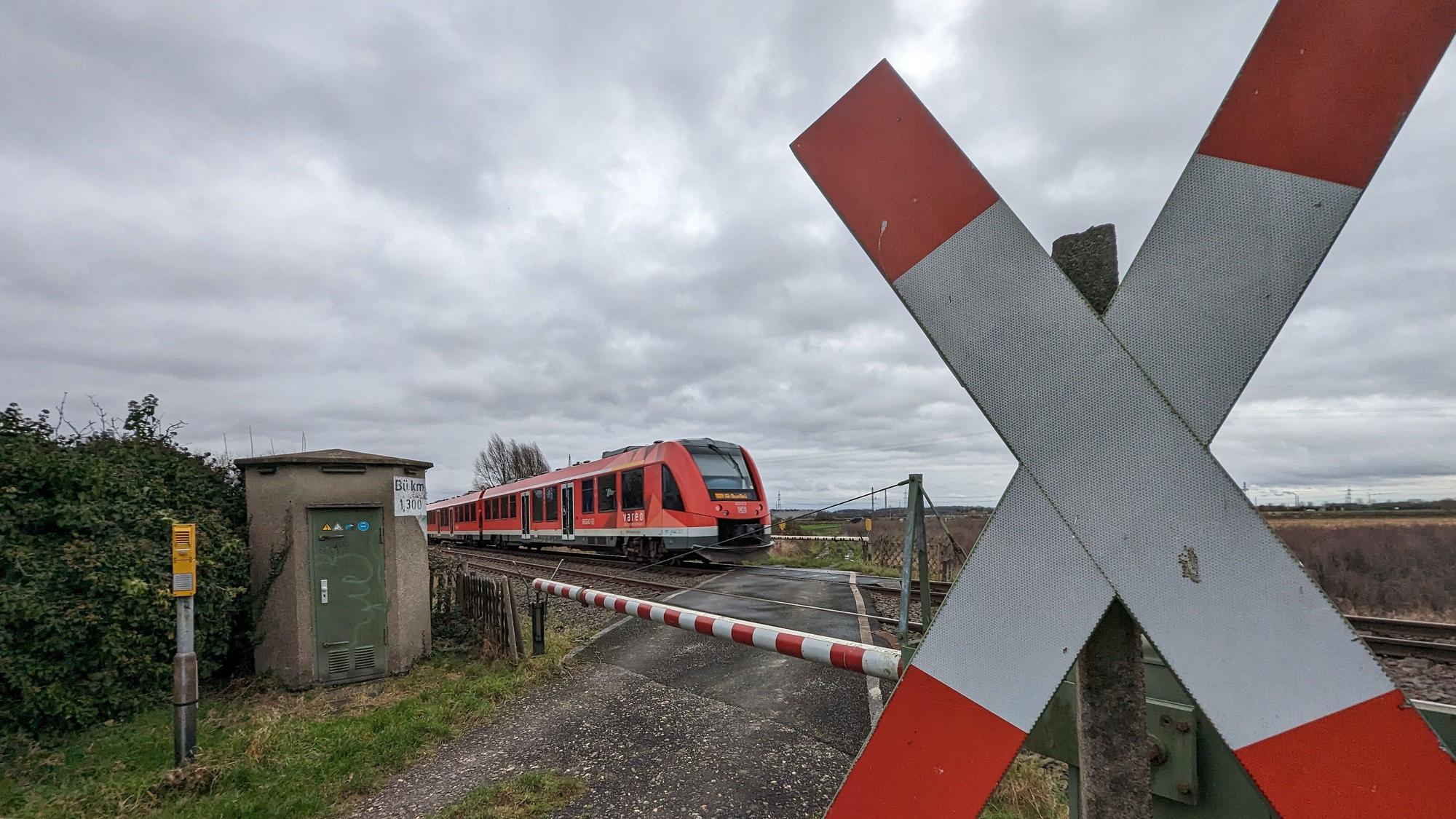 EIn Zug fährt an einem beschrankten Bahnübergang mit Andreaskreuz über das Gleis.