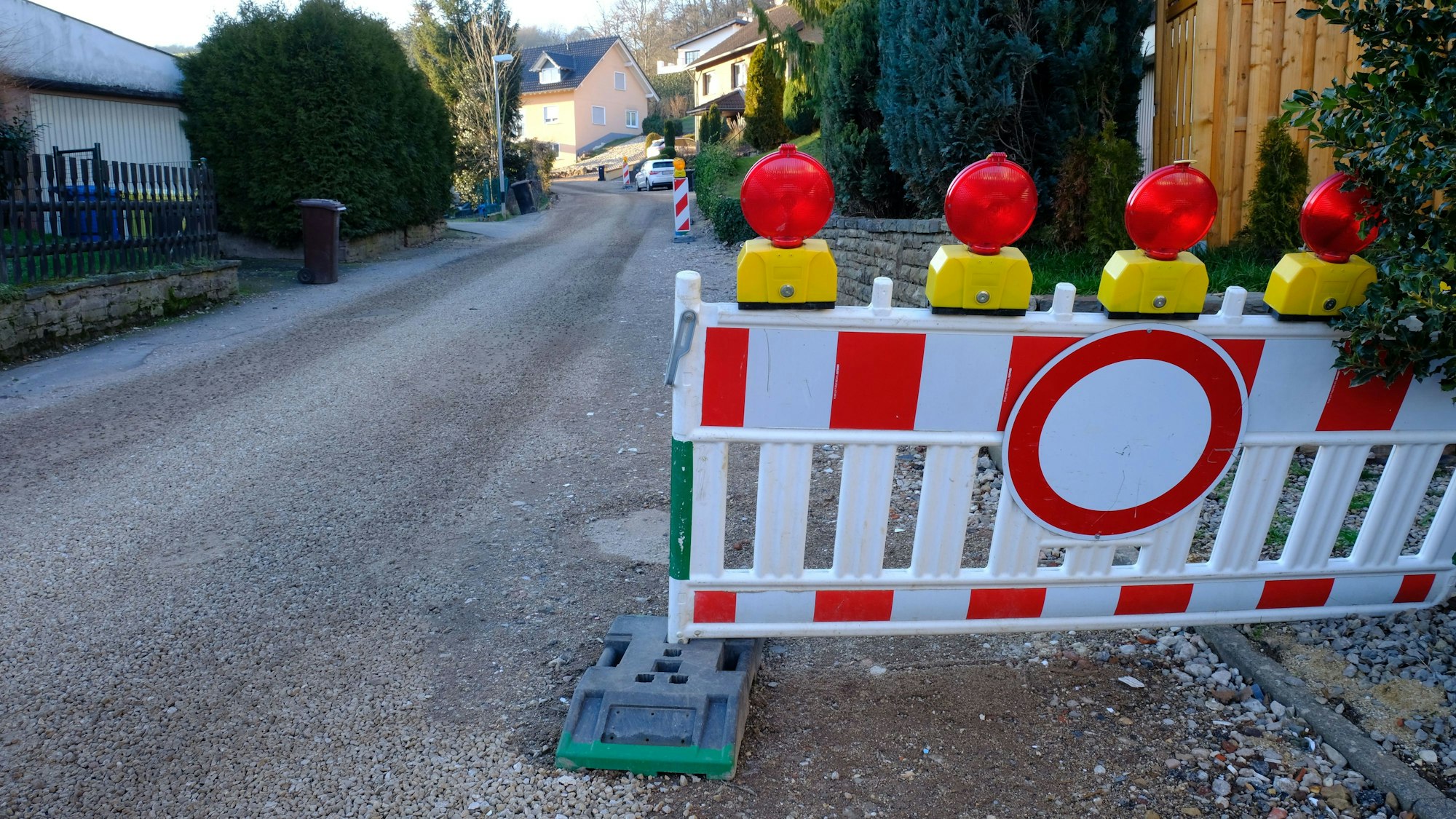 Auf der Baustelle im Höhenweg in Mechernich-Vussem ruhen aktuell die Bauarbeiten witterungsbedingt. Absperrbaken und die fehlende Teerdecke weisen darauf hin, dass die Straße ausgebaut wird.
