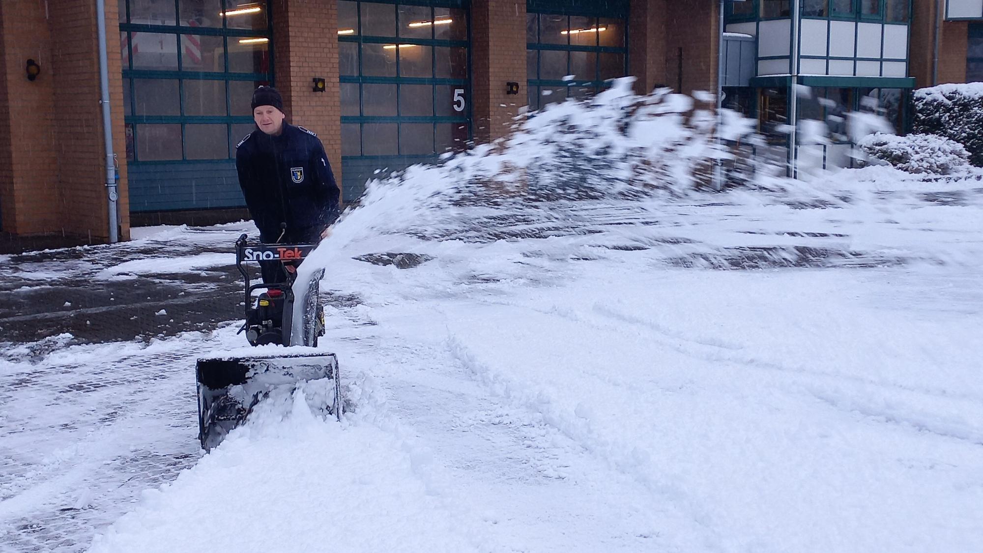 Ein Mann beseitigt mithilfe einer Schneefräse den Schnee auf dem Hof vor einer Feuerwehrwache.